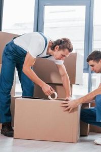 packaging-the-box-two-young-movers-in-blue-uniform-working-indoors-in-the-room-photo packaging-the-box-two-young-movers-in-blue-uniform-working-indoors-in-the-room-photo